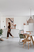 Woman walks through open-plan dining area with modern furnishings and pastel-coloured accents