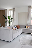 Light grey corner sofa with colourful cushions in modern living room with large plants and wooden panelling