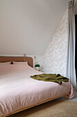 Attic bedroom with pink bed linen and wallpaper with leaf pattern