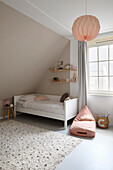 Bright children's room with sloping ceiling, bed and hanging lamp in pink