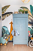 Blue wooden wardrobe in front of tropical wallpaper in the nursery