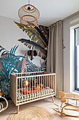 Modern nursery with jungle wall mural, wooden cot and rocking horse