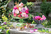 Blumenarrangement mit Rosen und Hagebutten auf rustikalem Holztisch im Garten