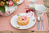 Table setting with china and cake on pink tablecloth in the garden