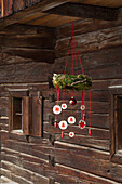 Advent wreath with red and white ornaments hangs in front of a wooden hut