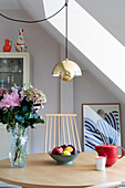 Round dining table with glass vase, fruit bowl and golden pendant light