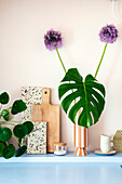 Monstera leaf and ornamental leek (allium) in striped vase