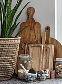 Wooden chopping boards and storage jars next to a woven basket with houseplant