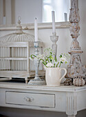 Shabby chic decor with candlesticks, birdcage and flower vase on sideboard