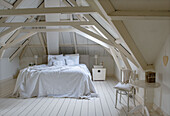 Bedroom in the attic with exposed wooden beams in white and minimalist furnishings