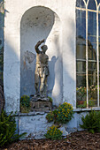 Stone figure in niche with ferns and flowering shrubs