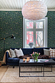 Living room with blue velvet sofa, patterned wallpaper and feather lamp