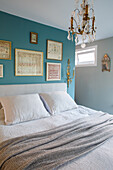 Bett mit Leinenbettwäsche vor petrolfarbener Wand mit gerahmten Stickbildern