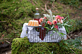 Picknickkorb mit Likör, Kuchen und Blumen im Wald