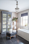 Bathroom with bathtub, chandelier and grey display cabinet