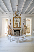 Bright living room with wooden ceiling, angel statues and benches in front of marble fireplace