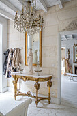 Baroque-style console with Madonna statue and chandelier in light-coloured hallway