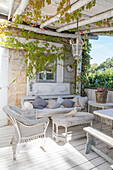 Covered terrace with light-coloured rattan furniture and climbing plants