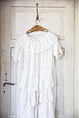 White summer dress on wooden hanger in front of old-fashioned door