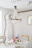 Chandelier and antique grandfather clock in the white dining room in shabby chic style