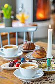 Coffee table with cappuccino, chocolates and biscuits in front of a fire