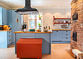 Kitchen with blue cupboards, wooden chest in rust red and brick wall with oven