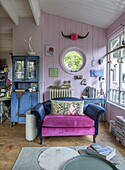 Living room with pink and blue sofa, display cabinet and round window opening