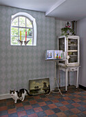 Corner of room with diamond wallpaper, antique glass cabinet and cat on the floor