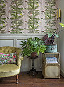 Mustard yellow armchair and potted plants in front of Art Nouveau wallpaper in the living room