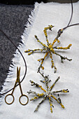 DIY-Sterne aus Zweigen und Flechten auf Textiluntergrund neben Schere
