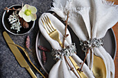 Festive table decoration with gold-coloured cutlery and napkin rings made from natural materials
