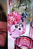 Pink carnation and sloe berries on a branch in a glass