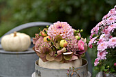 Autumnal arrangement with ornamental pumpkin vase, hydrangea flowers, dahlias (Dahlia), ornamental apples and apples on wooden table