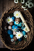 Dyed Easter eggs in shades of blue and natural colours with white flowers in a wicker basket