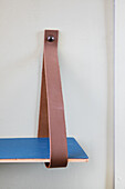 Wall shelf with blue wooden panel and brown leather strap