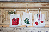 Drei Stofftaschen mit weihnachtlichen Applikationen vor Holzhintergrund