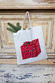 Fabric bag with gift appliqué and fir branches in front of a wooden door