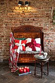 Antique vintage wooden bench with red accent cushions and candles in front of a brick wall