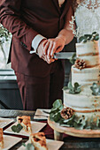 Bride and groom cutting wedding cake with eucalyptus decoration