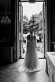 Braut im langen Kleid steht vor geöffneter Tür mit Blick in den Garten