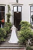 Braut in weißem Kleid steigt Steintreppen eines historischen Gebäudes hinauf
