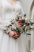 Bride in white dress holds colorful wedding bouquet