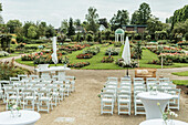 Freiluft-Hochzeitszeremonie im Rosengarten mit weißer Bestuhlung