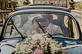 Brautpaar küsst sich im mit Blumenarrangement geschmückten Oldtimer