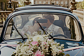 Bride and groom kissing in a vintage car decorated with floral arrangements