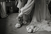 Braut zieht Sandalen mit Schleifen an unter fließendem Hochzeitskleid