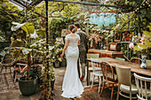 Bridal couple in a rustic greenhouse with dining table and plants