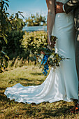 Bride holding bouquet, hands of groom, surrounded by nature
