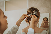 Frau steckt Haarschmuck in die Hochsteckfrisur einer Braut