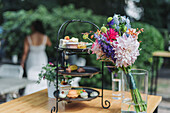 Dreistöckige Etagere mit Gebäck und Pralinen, bunter Blumenstrauß im Glas